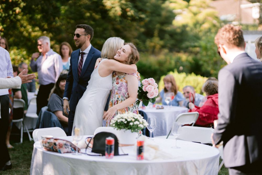 Guests mingle around white-clothed tables at an outdoor wedding reception.