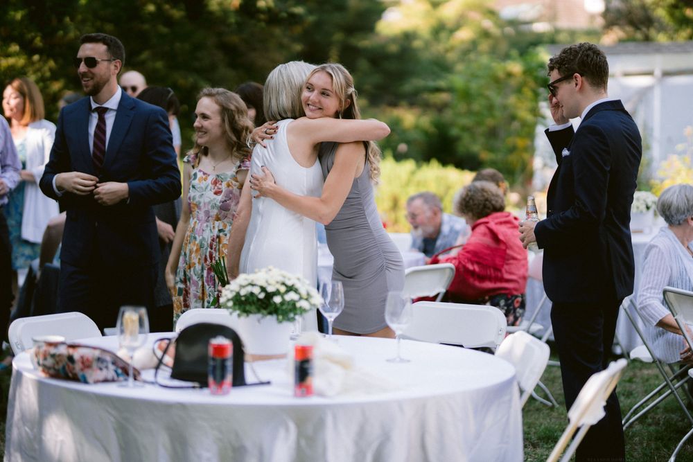 Wedding reception guests gather around decorated tables in an outdoor garden setting.
