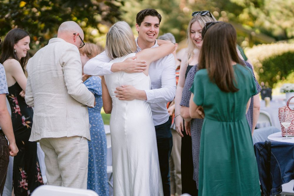 Wedding guests celebrate and embrace at an outdoor reception with tables visible.