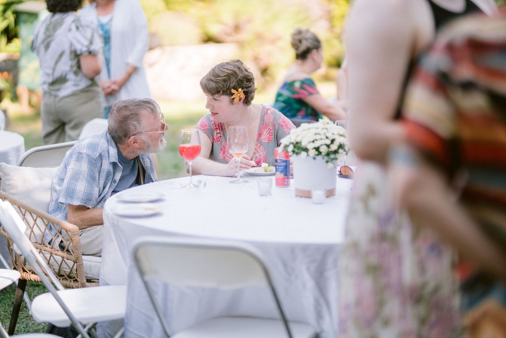 Intimate conversation between guests at an outdoor table during a garden party celebration.