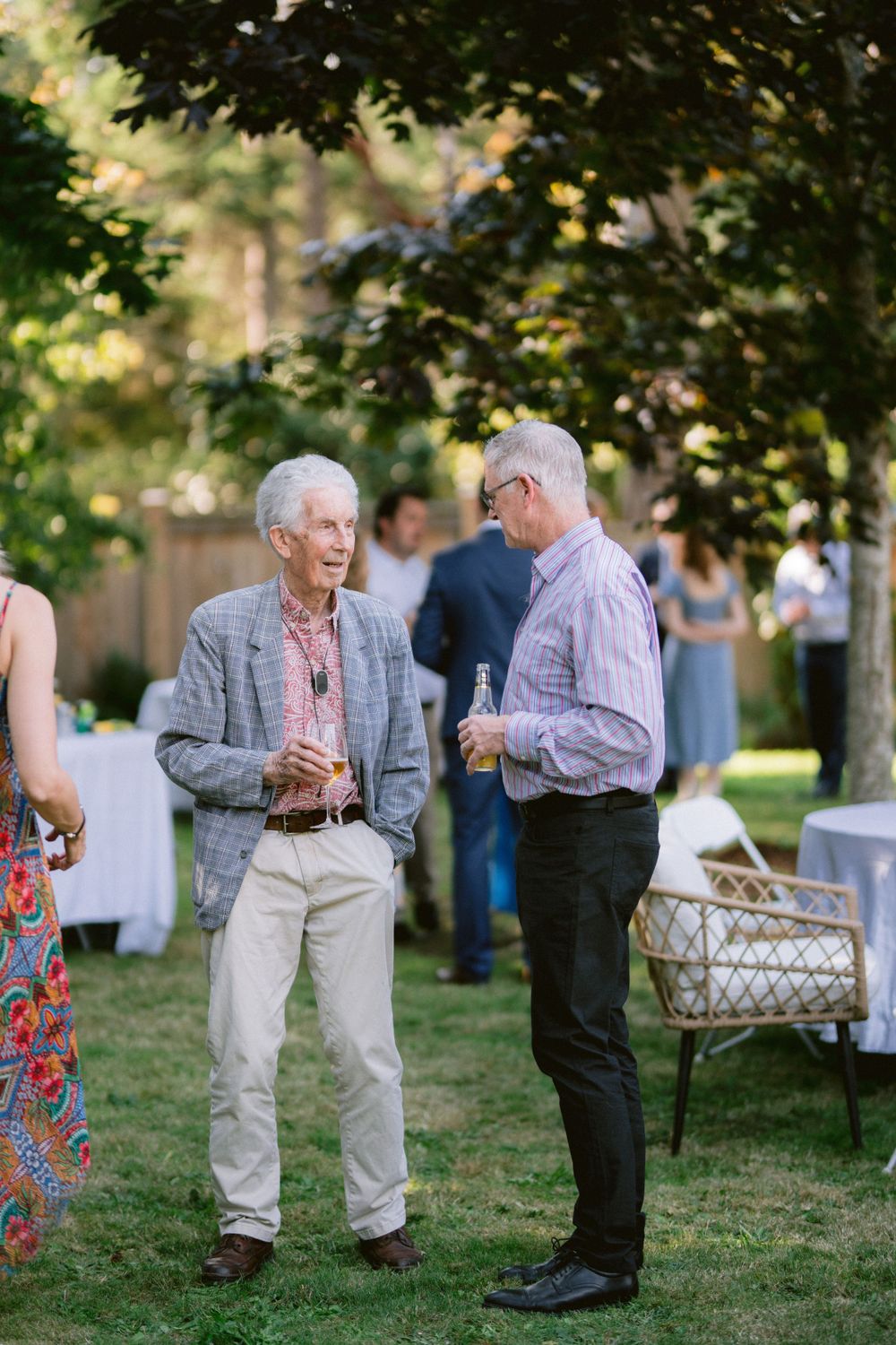 Two guests having a conversation under trees at an outdoor reception.