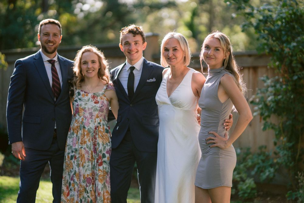 Group photo of wedding attendees in formal attire in a garden setting.