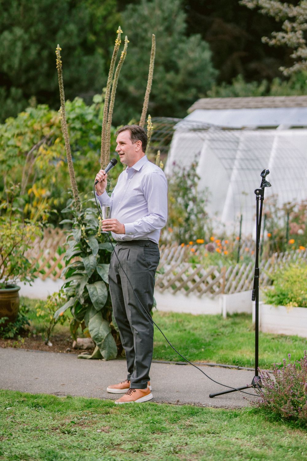 Speaker in light colored shirt delivering remarks near garden greenhouse.
