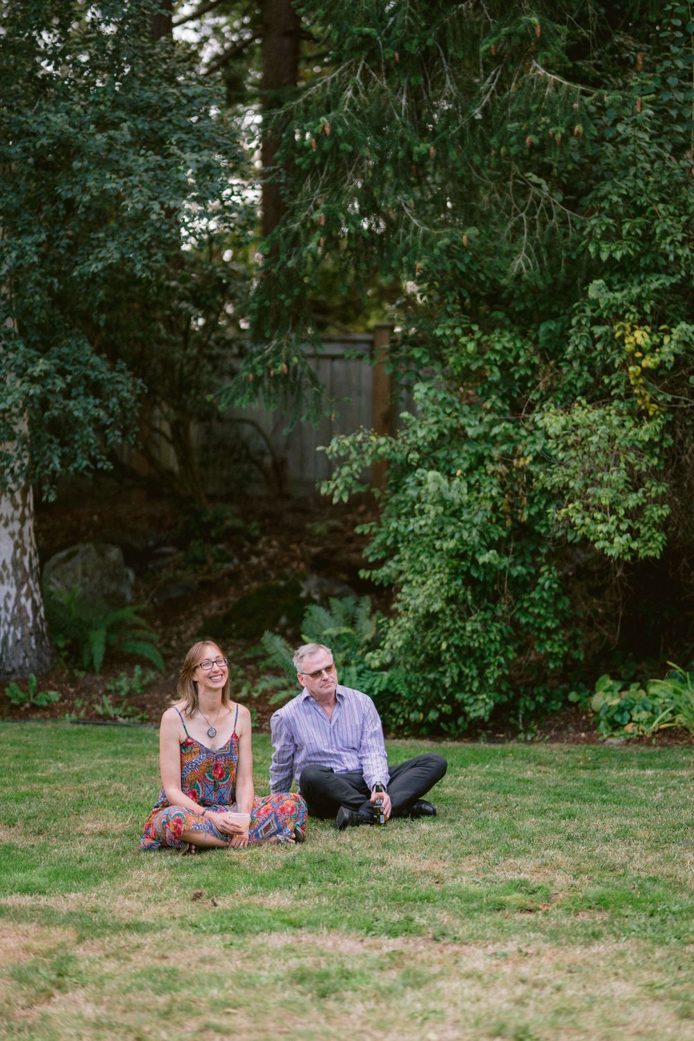 Two people sitting casually on grass in garden setting.
