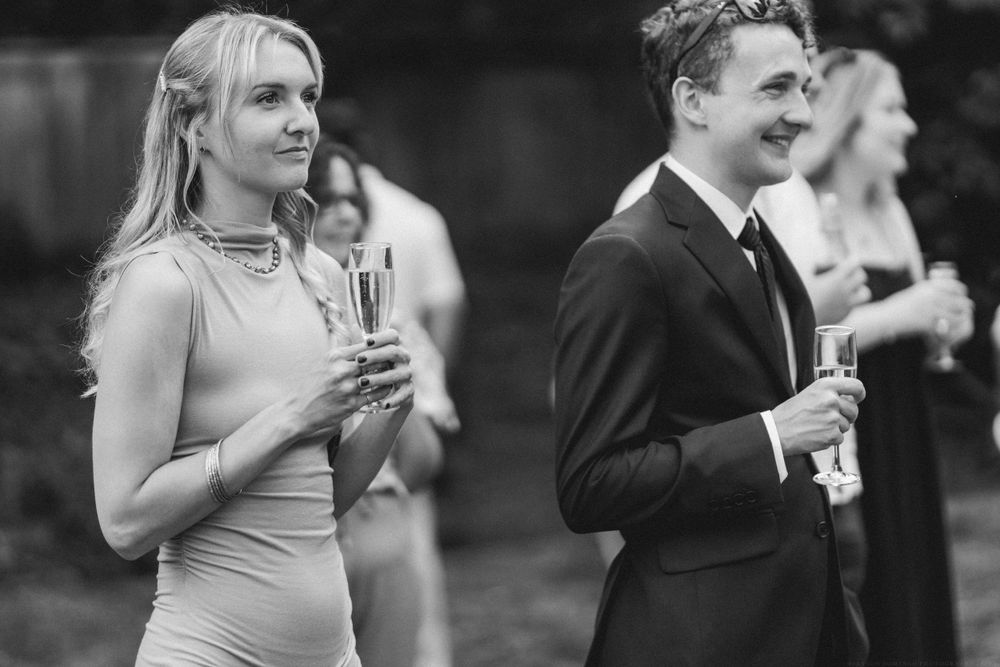 Black and white photo of guests holding champagne glasses at outdoor event.