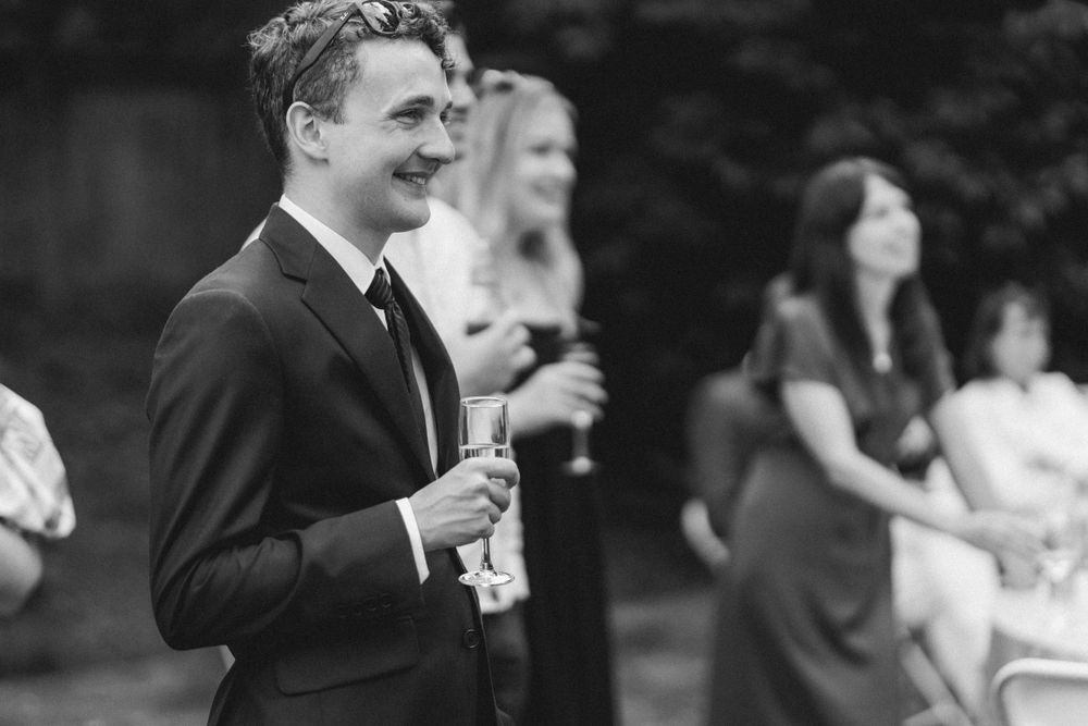 Man in suit smiling while holding drink at outdoor gathering.