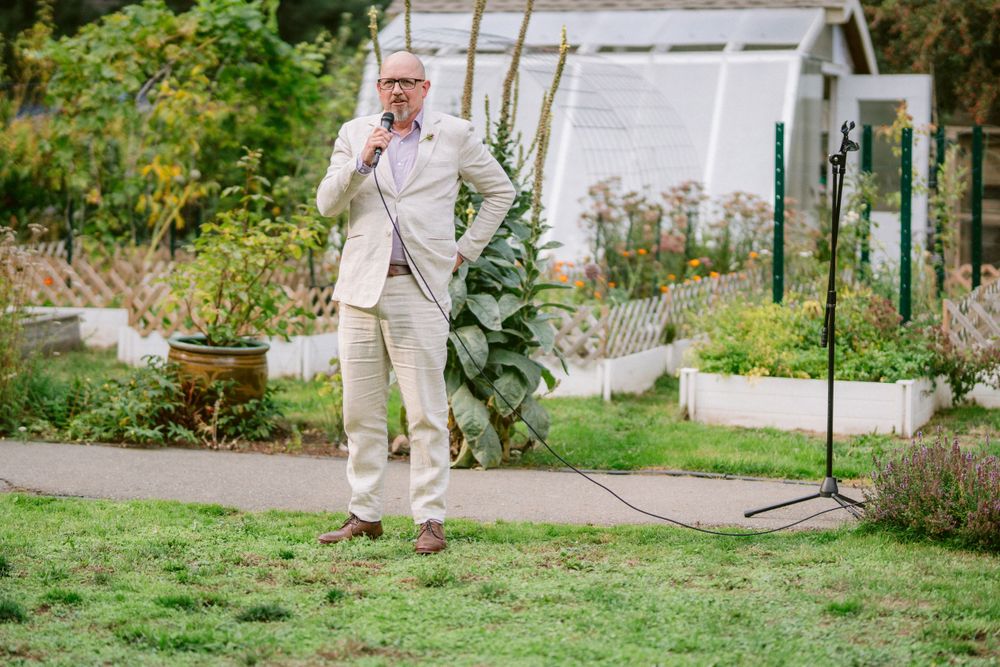 A person in a light beige suit stands alone in a lush garden setting.