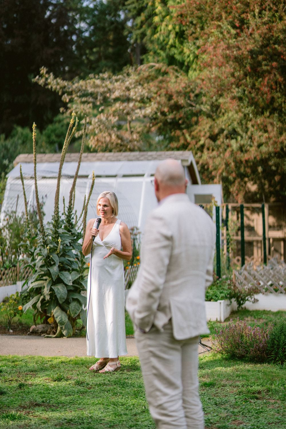 Two people share a heartfelt moment in a garden with a white greenhouse in the background.