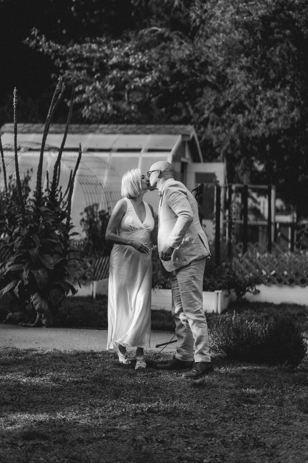 A romantic black and white photo of a couple sharing their first kiss in a garden setting.