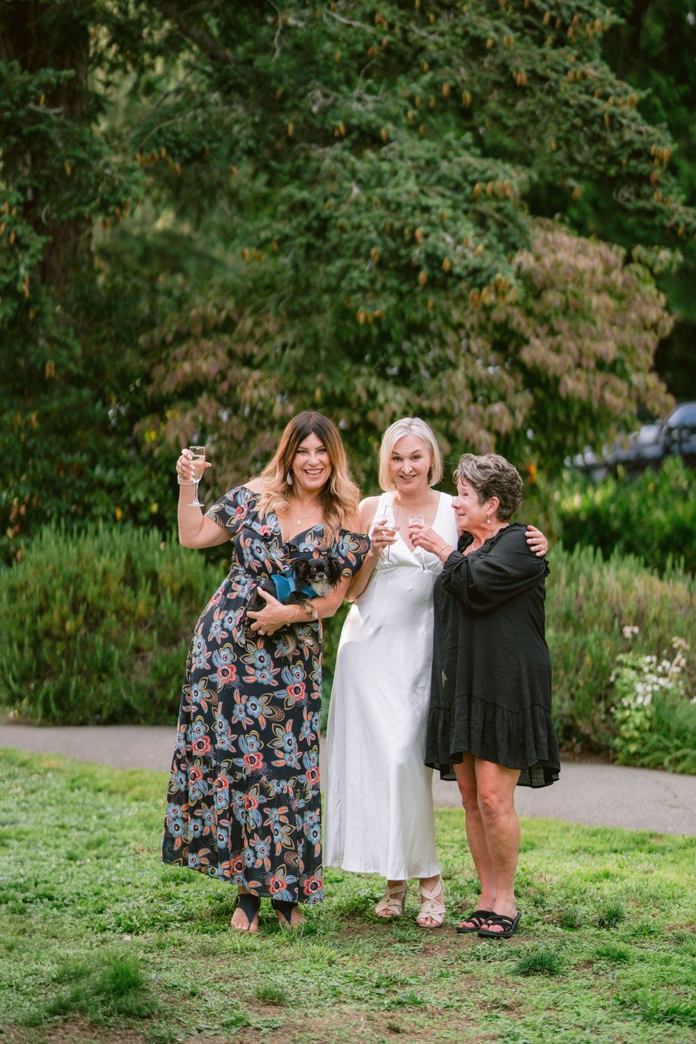 Three guests celebrate joyfully on a garden lawn during a wedding reception.
