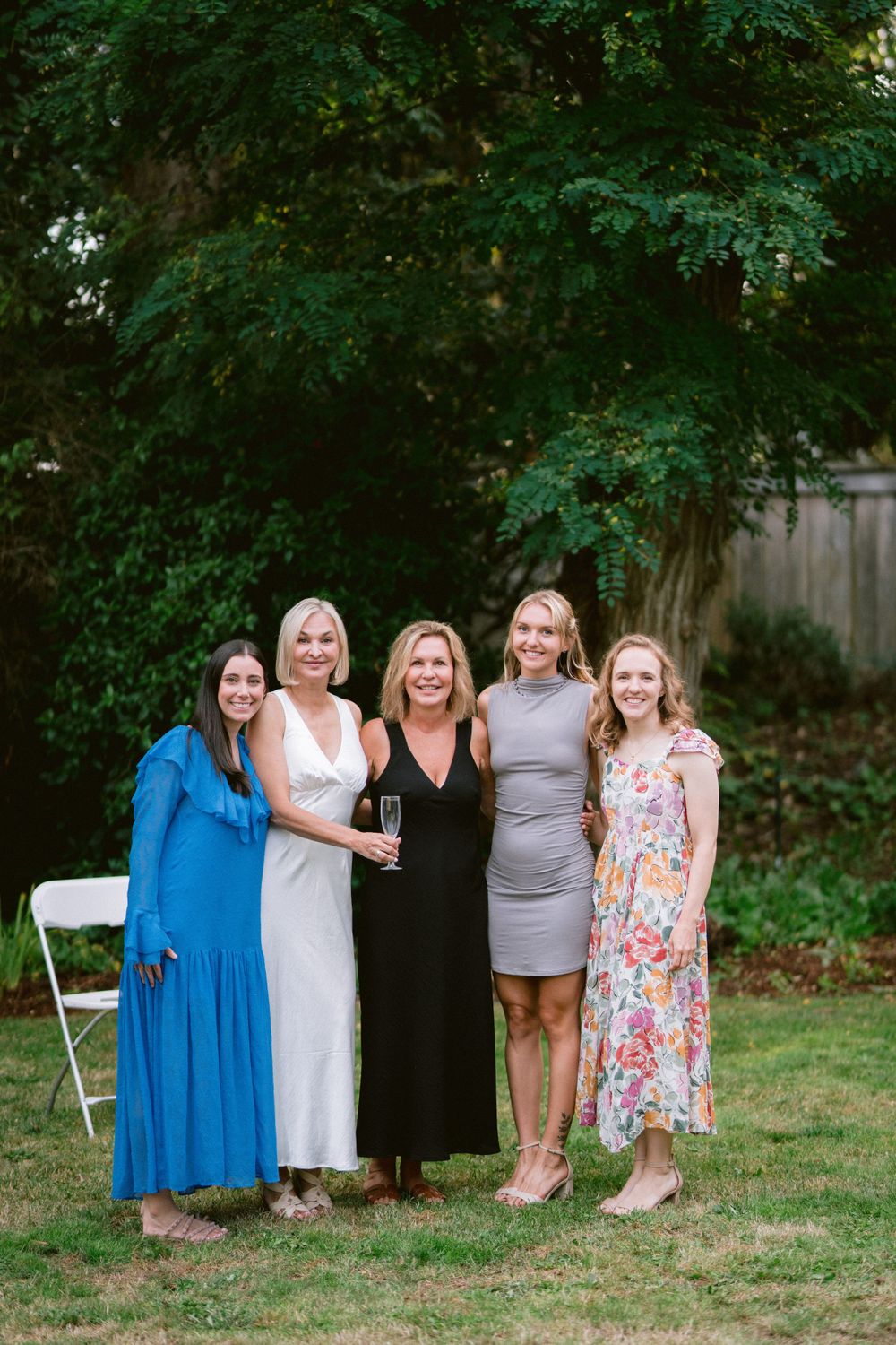 Five people pose together for a group photo on a lawn with green trees in the background.