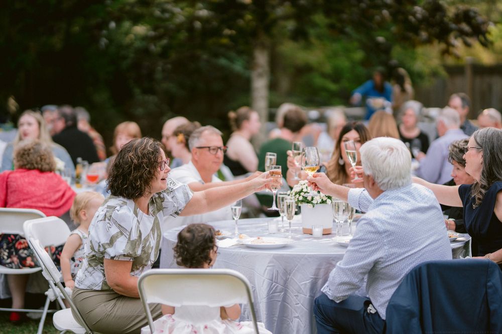 Wedding guests enjoy dinner at round tables during an outdoor reception.