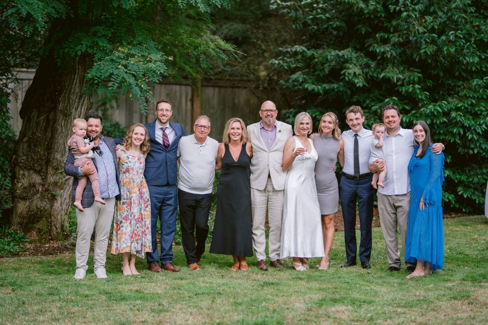 A group of guests in summer attire stand together for a photo on a lush green lawn.