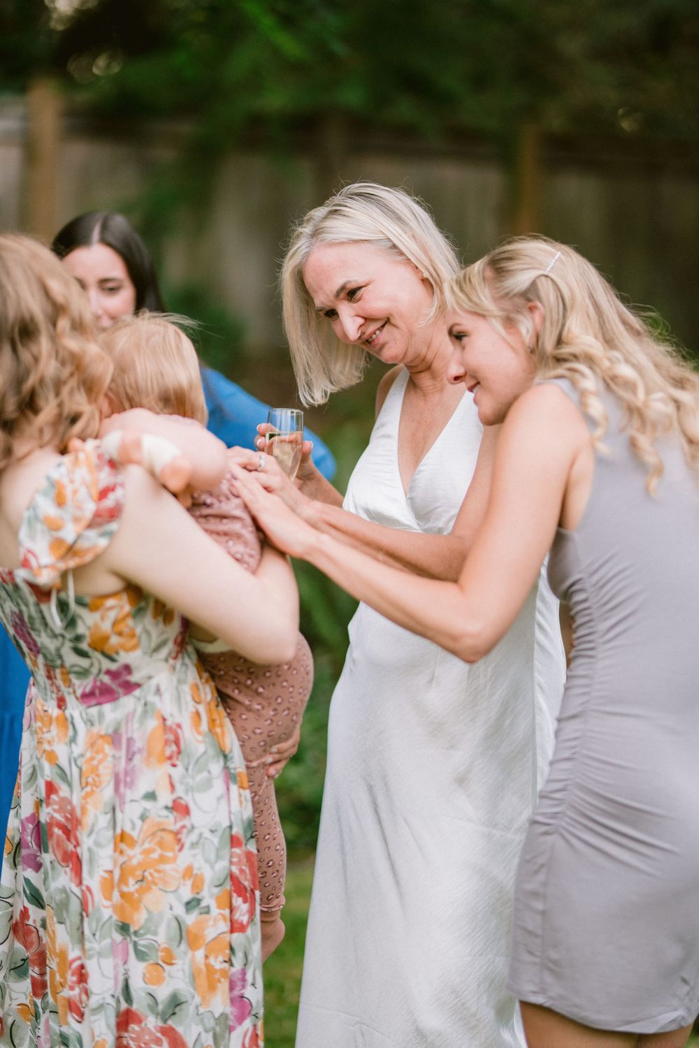 Three people share a joyful moment while looking at something on a sunny day outdoors.