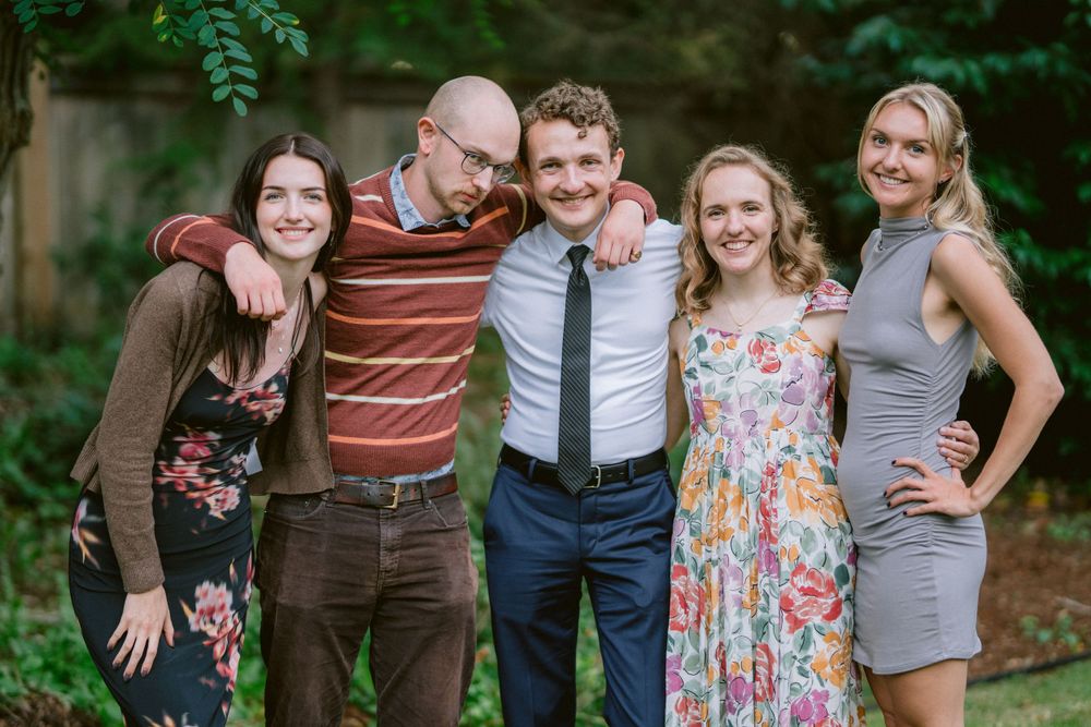Five people stand together for a group photo in a backyard garden setting.