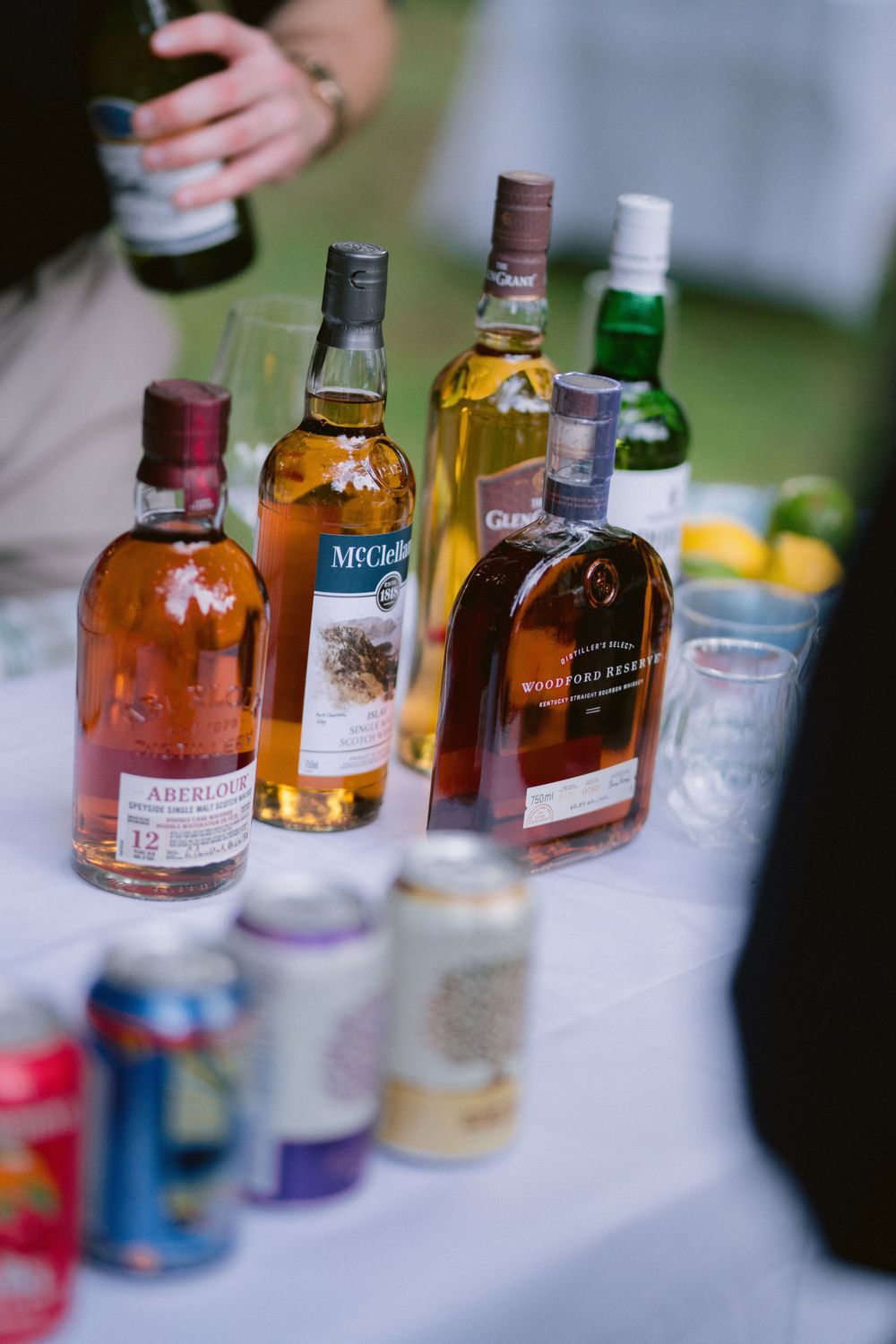 Various bottles of liquor and mixers arranged on a white tablecloth at an outdoor event.