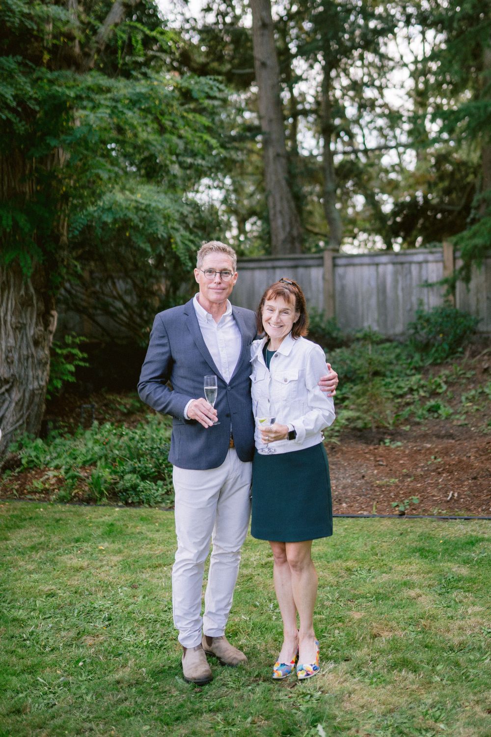 A well-dressed couple shares a celebratory moment while holding drinks in a garden setting.