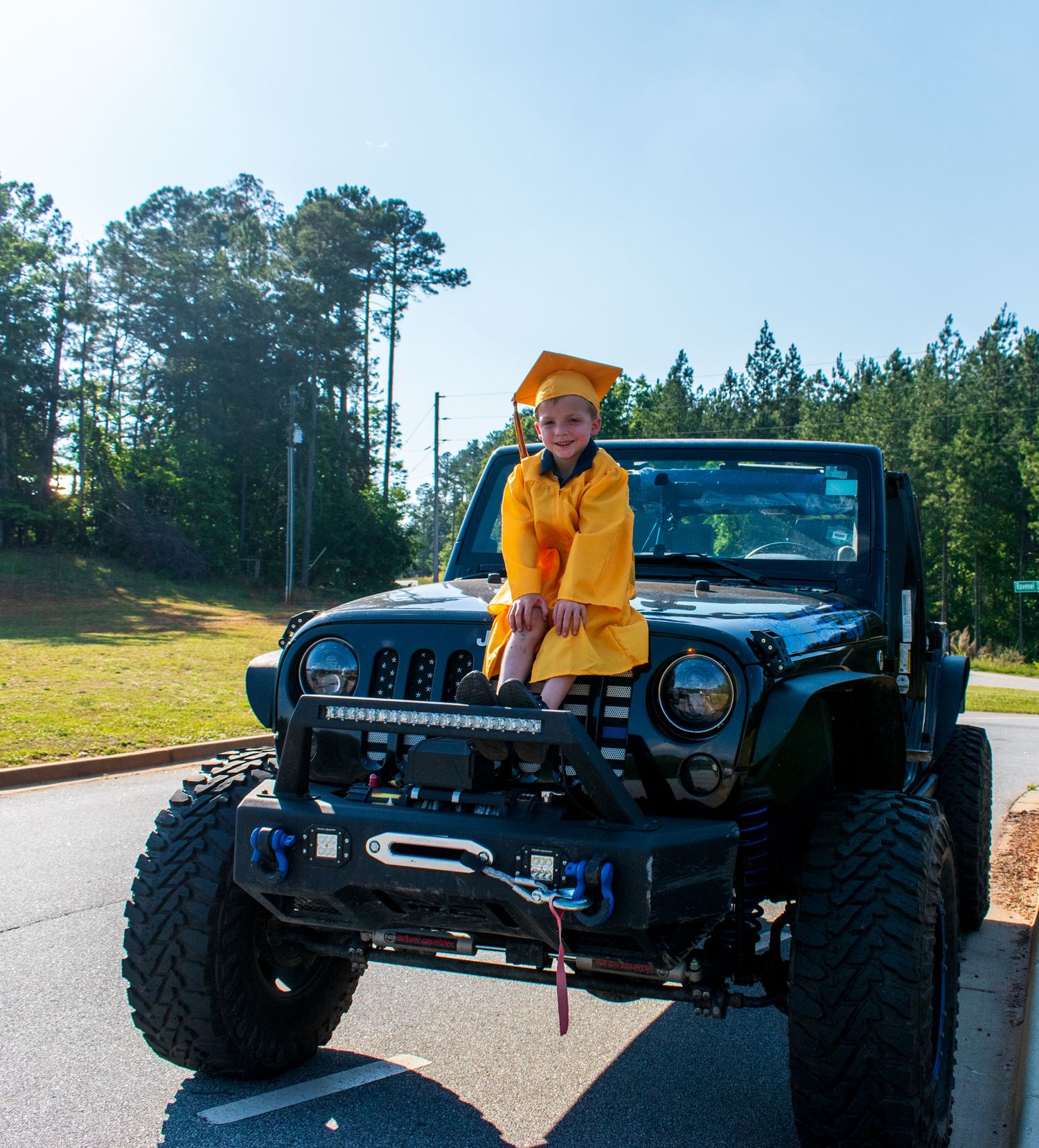 Child in bright yellow jacket standing on modified black Jeep Wrangler.