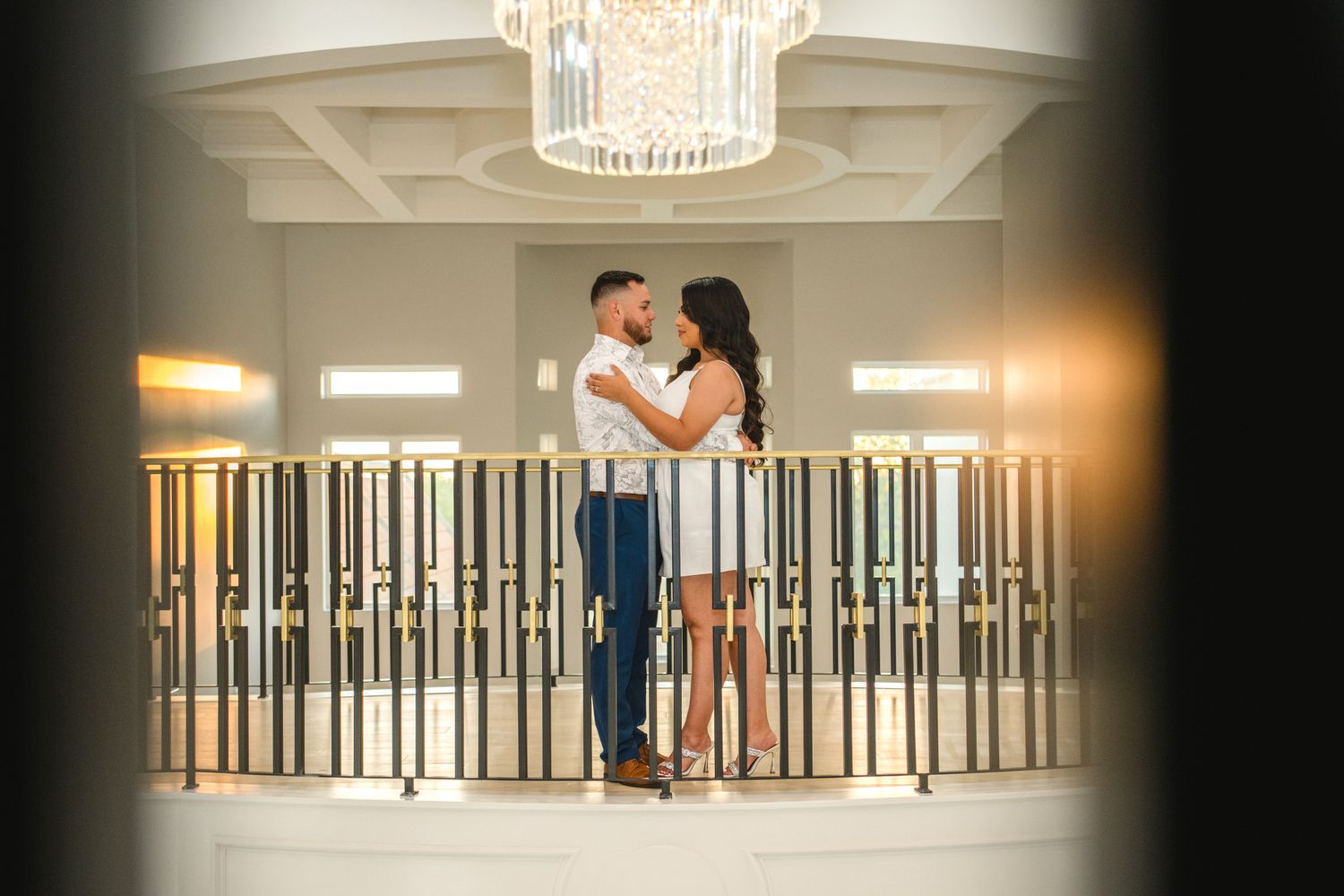 Couple dancing together in an elegant ballroom setting with crystal chandeliers and ornate railings.