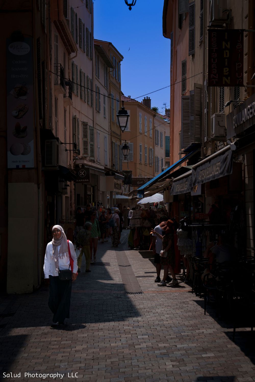 Narrow cobblestone street with traditional buildings and shops in a charming European town during daytime.