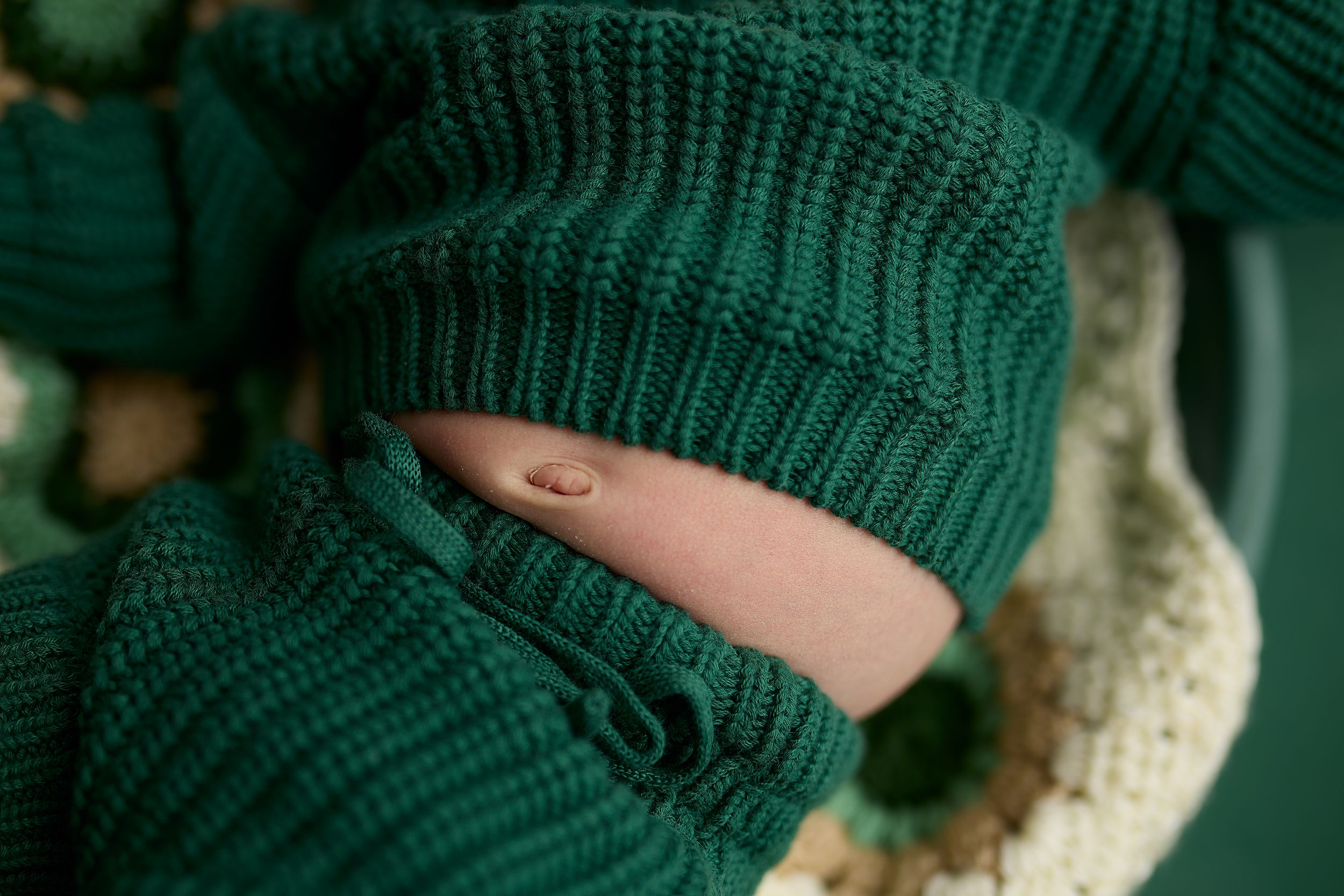 Close up detail of a dark green knit sweater sleeve showing ribbed texture and button detail.
