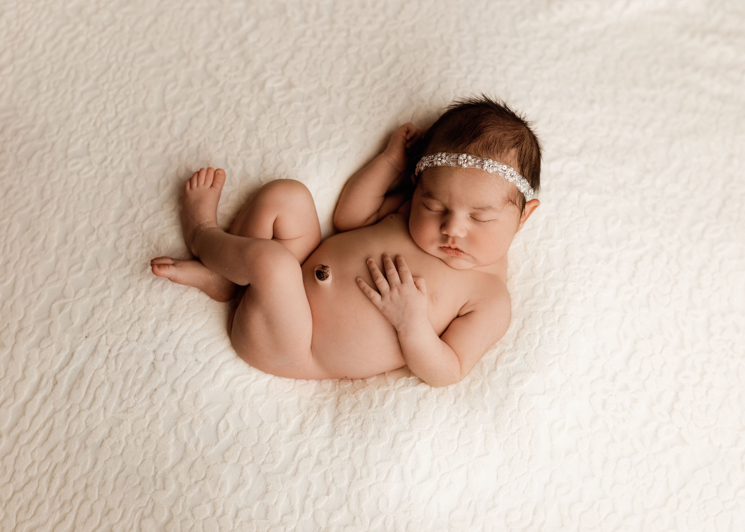 Peaceful newborn baby girl sleeping on white fluffy blanket wearing a delicate floral headband.