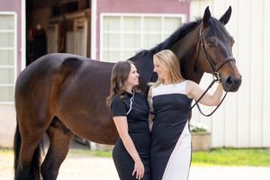 two girls in cocktail dresses looking at each other with large bay horse