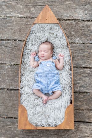 Newborn photo of a baby in a wooden boat lying on a fuzzy rug