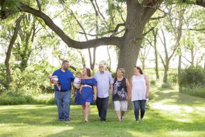 Large family from infant to senior walking under a large tree through the grass