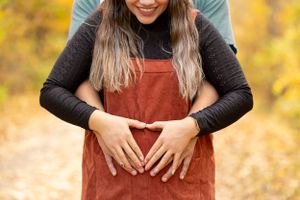 Couple making heart over baby bump in fall