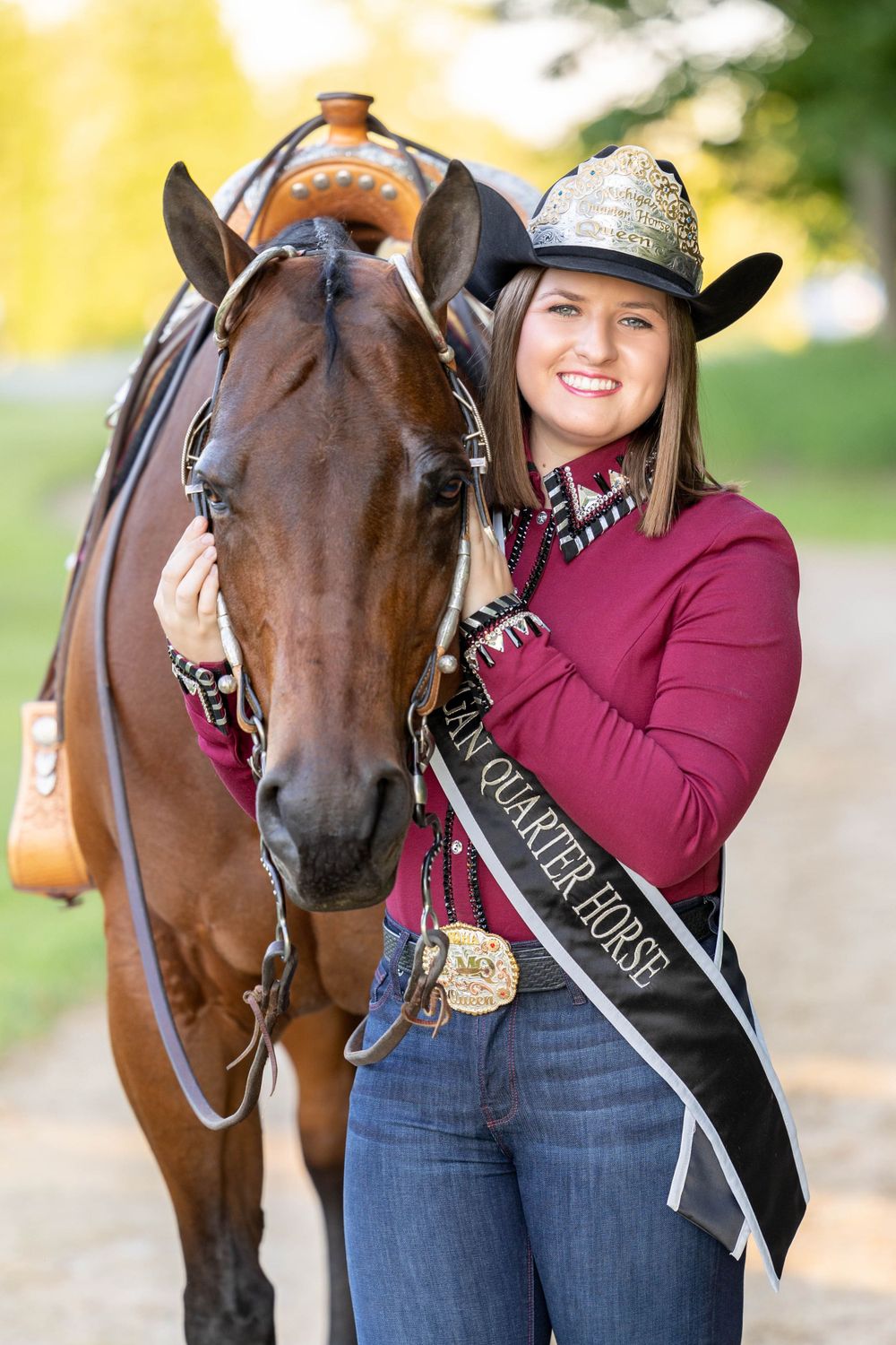 Michigan Quarter Horse Association Queen standing with her bay mare in a maroon horsemanship shirt with sash and crown