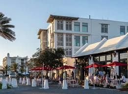 A panoramic view of coastal buildings and palm trees along a beachfront street with red umbrellas and pedestrians.