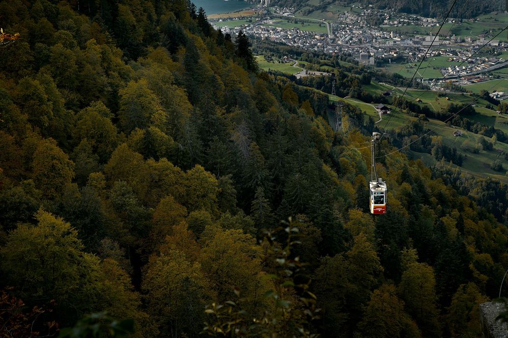 Aerial view of a town nestled in a lush green valley surrounded by forested mountains on a sunny day.