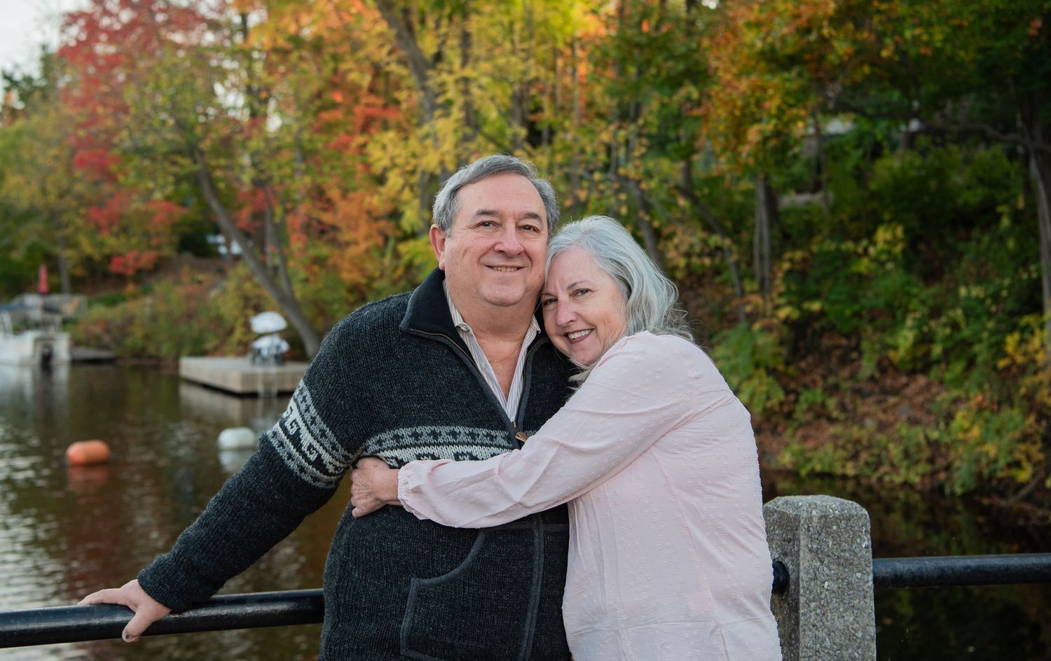 Couple shares romantic moments together outdoors during autumn with colorful fall foliage in background.