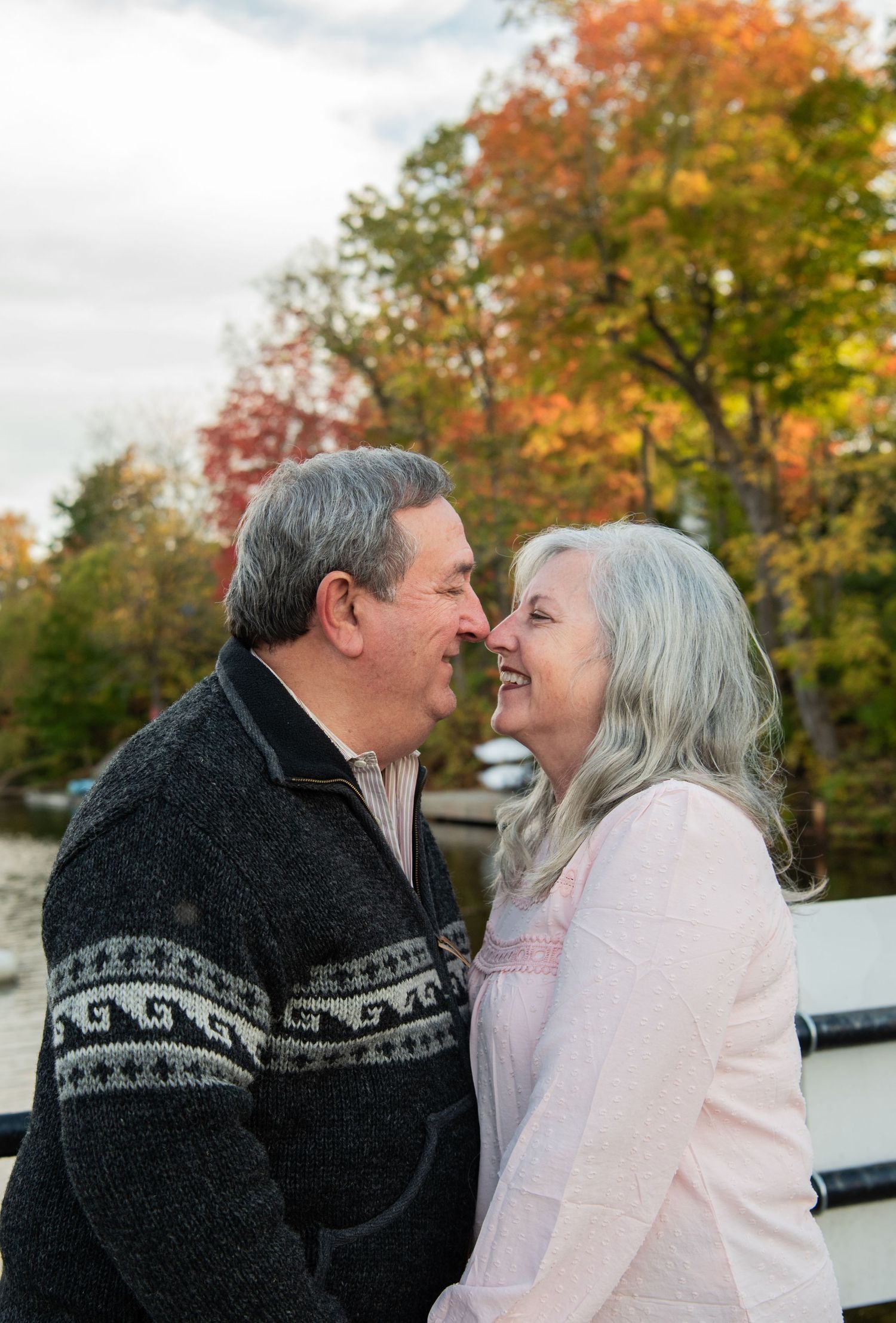 A loving couple shares a tender moment outdoors during autumn with colorful fall foliage in the background.