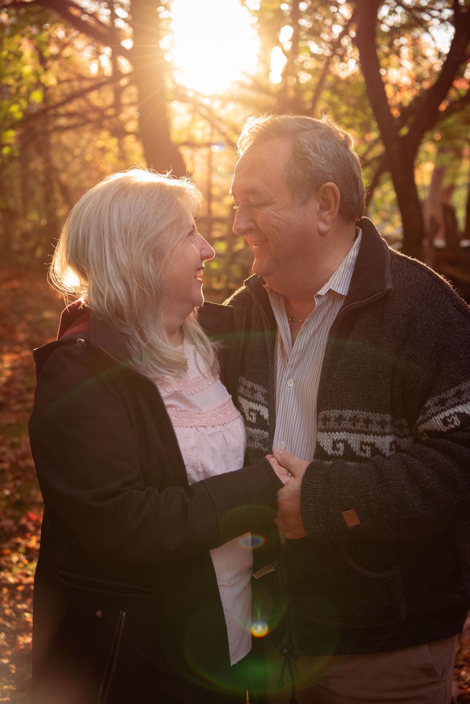 Senior couple sharing a romantic moment outdoors at sunset with golden sunlight filtering through autumn trees.