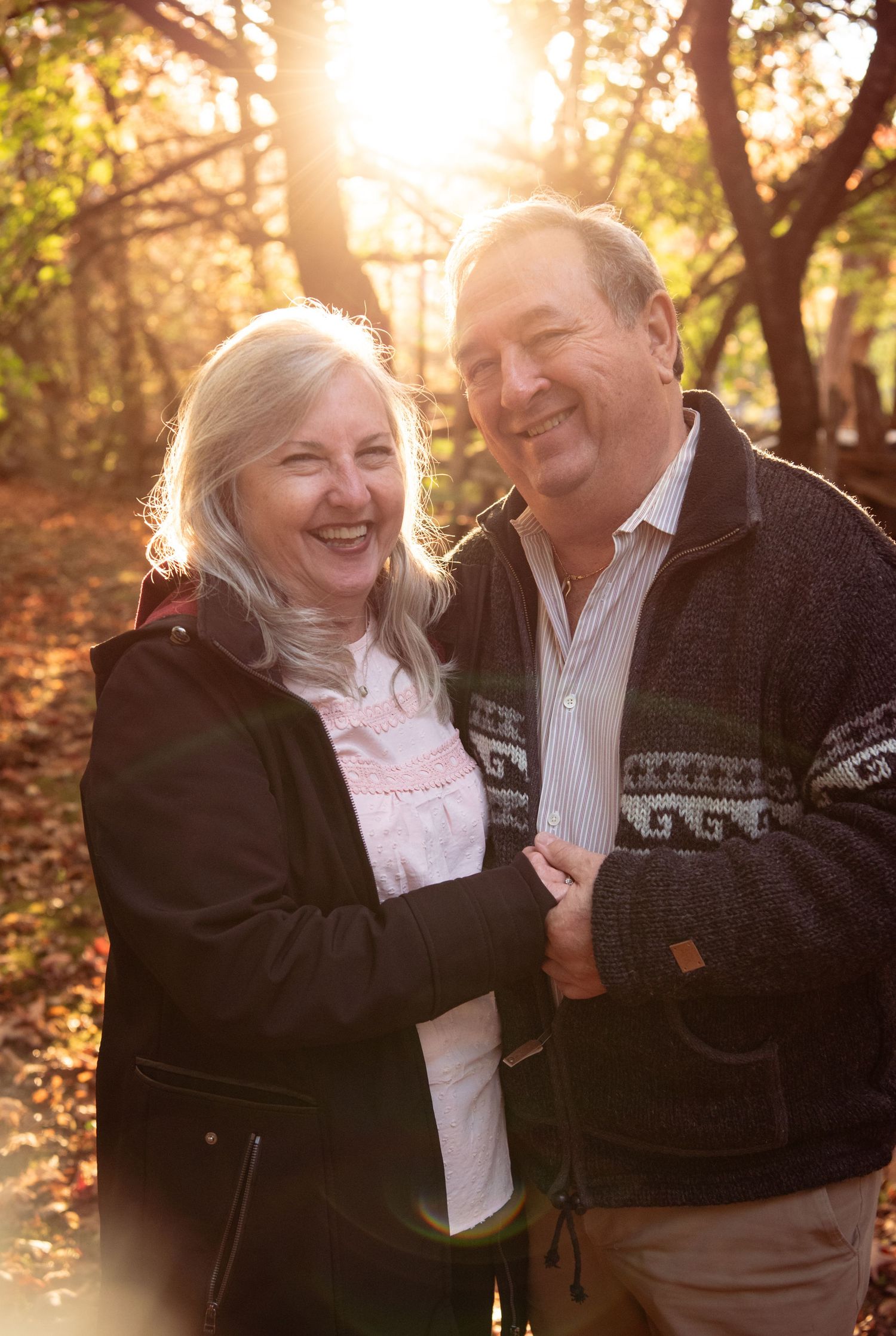 A couple shares joyful laughter together during a romantic autumn photoshoot in a sunlit forest setting.
