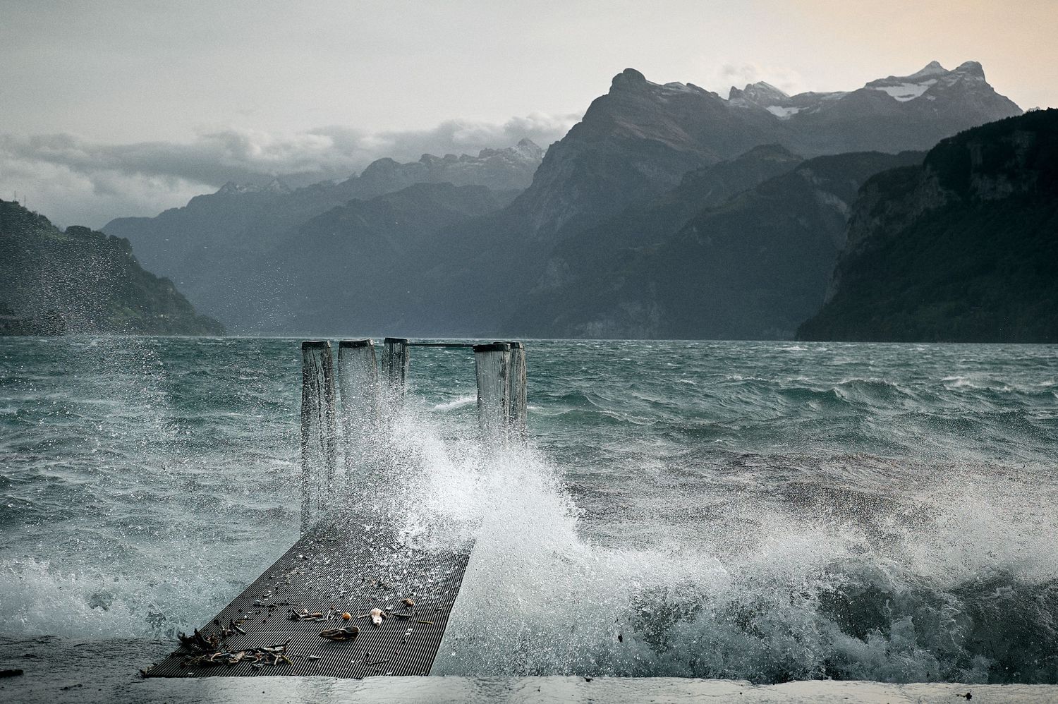Dramatic sequence of waves crashing against a pier with misty mountains in the background during stormy weather.