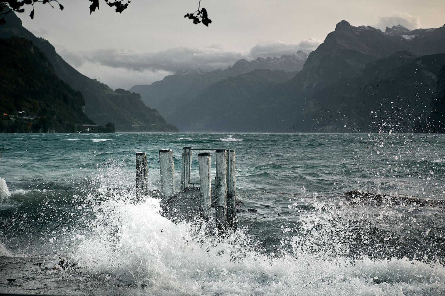 Dramatic ocean waves crash against coastal rocks and pillars during stormy weather at a rugged shoreline.