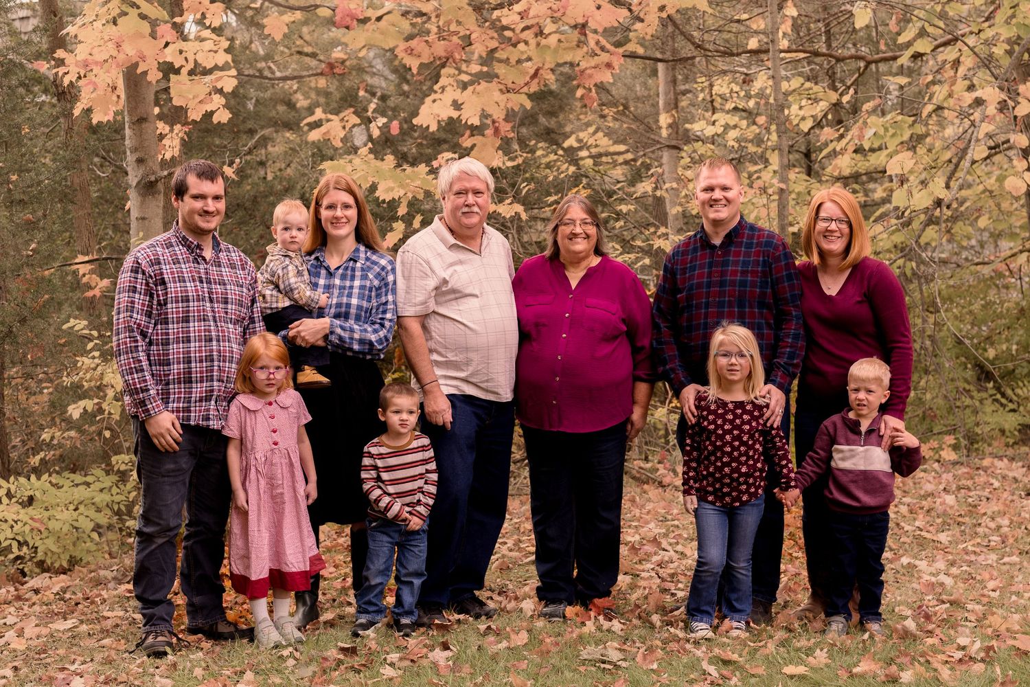 Extended family poses together for outdoor autumn portraits with colorful fall leaves.