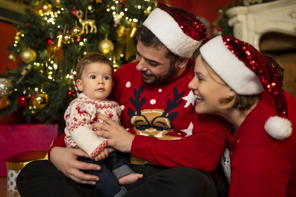 Una acogedora escena navideña con gente que lleva gorros de Papá Noel y jerséis festivos reunida junto a un árbol decorado.