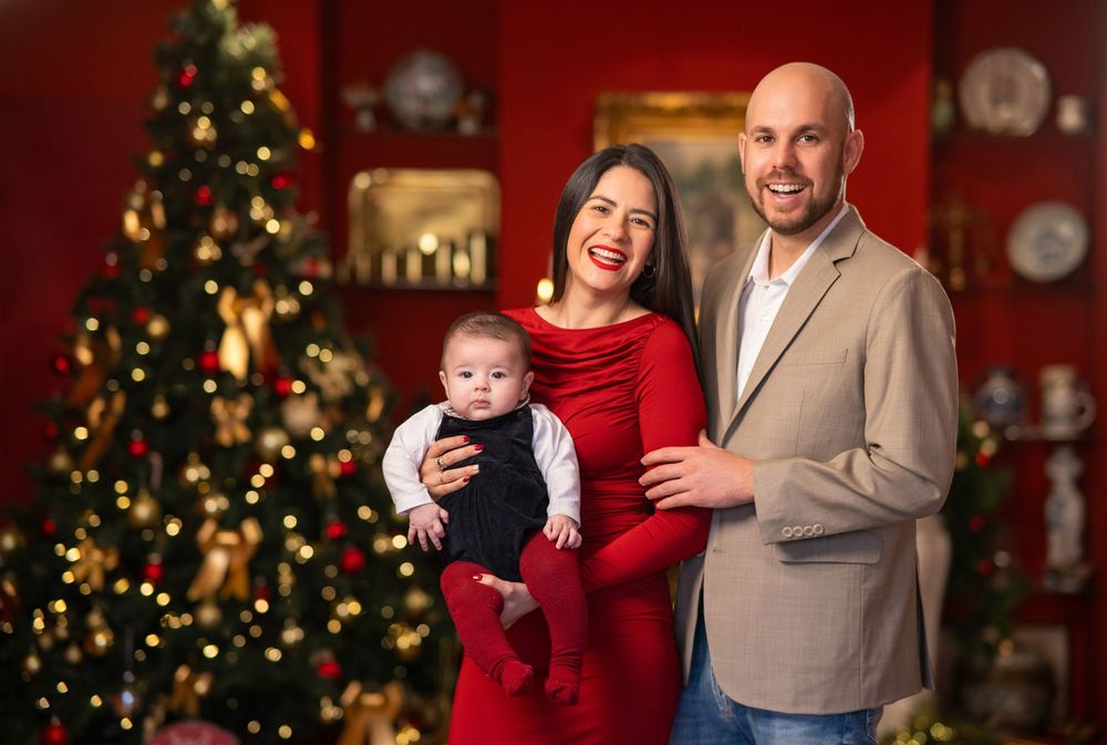 Familia con bebe posando en una decoracion de arbol navideño y chimenea con decoración navideña