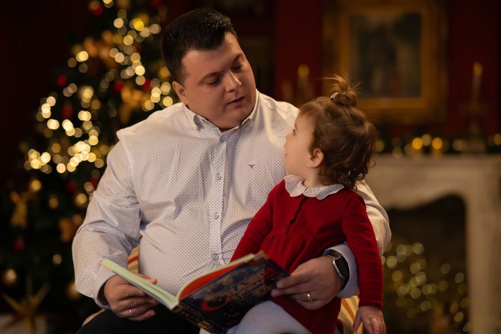 Padre leyendo uyn cuento navideño a su hija y un fondo navideño detrás