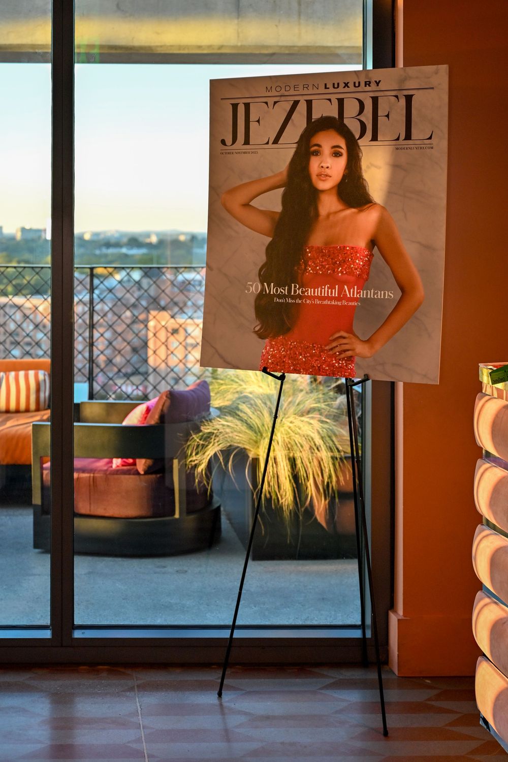 A magazine cover displayed on a stand near a window with a cityscape view and indoor plants.