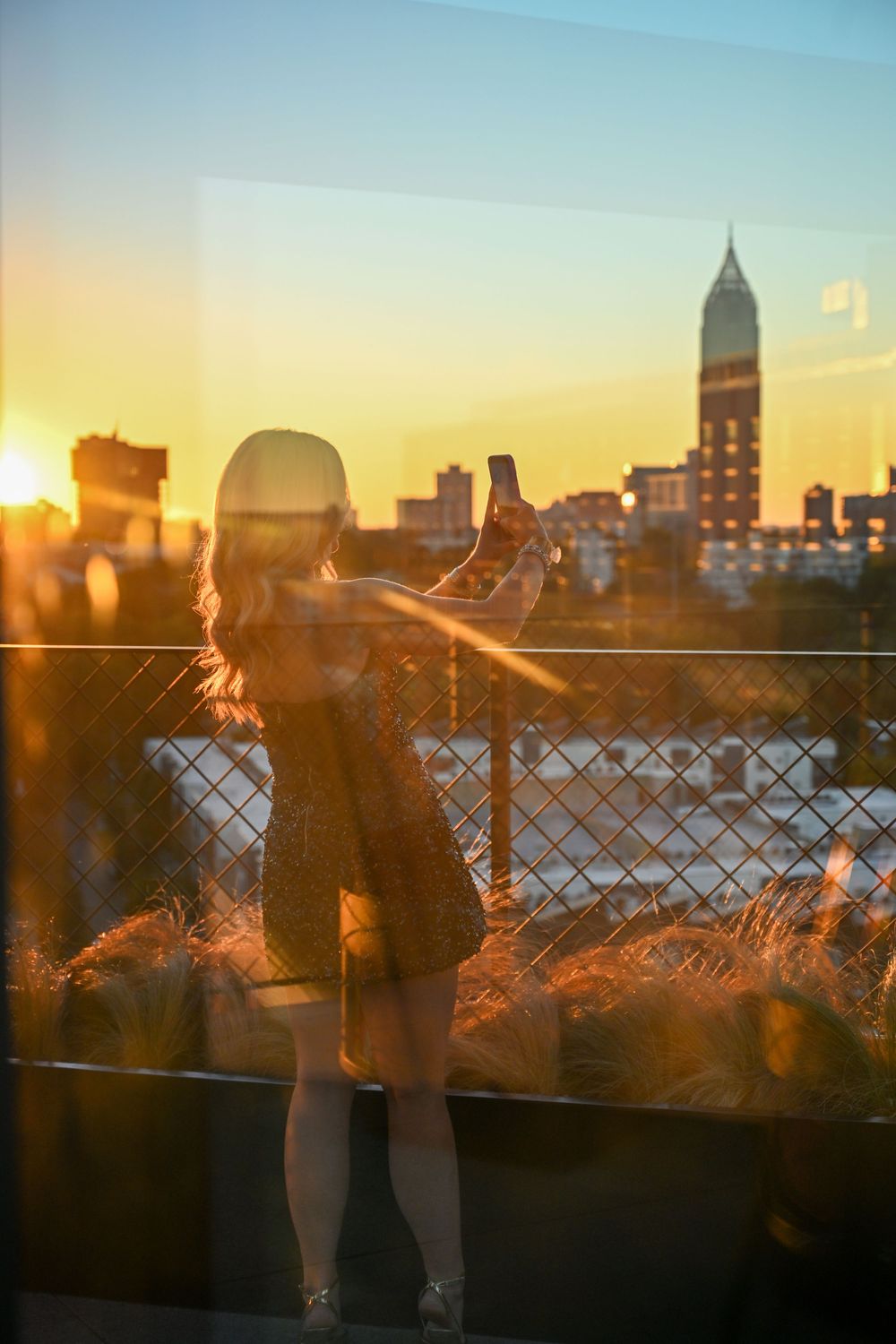Silhouettes against a golden sunset cityscape with urban buildings and a fence creating a romantic atmosphere.
