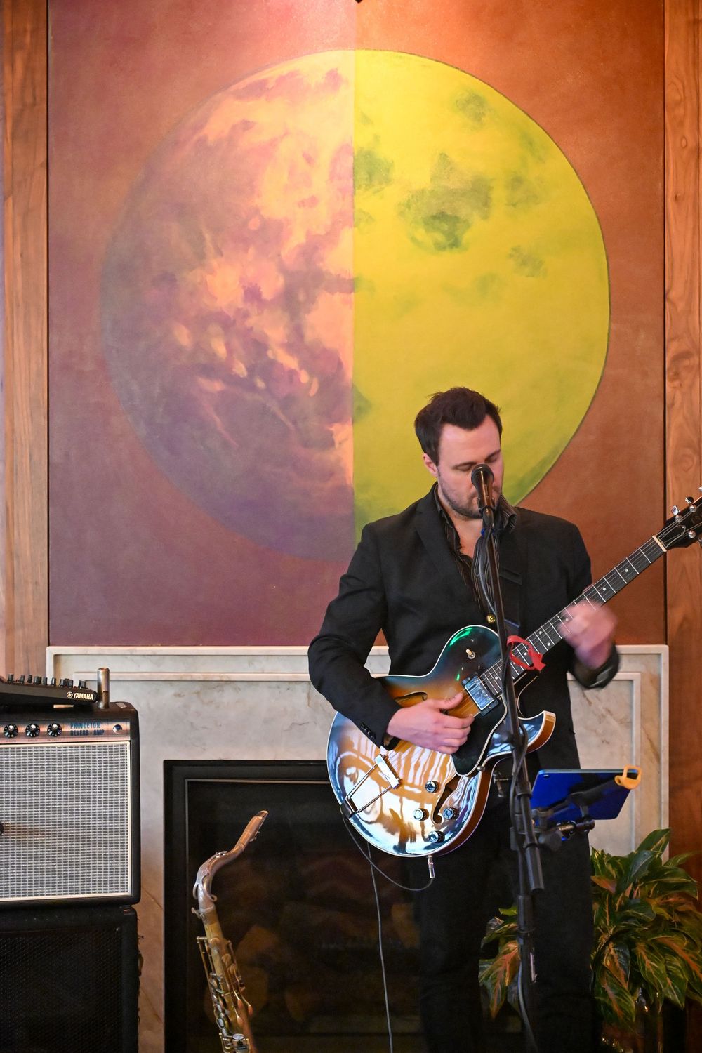 A musician performs with an electric guitar against a backdrop of large yellow and orange circular artwork.