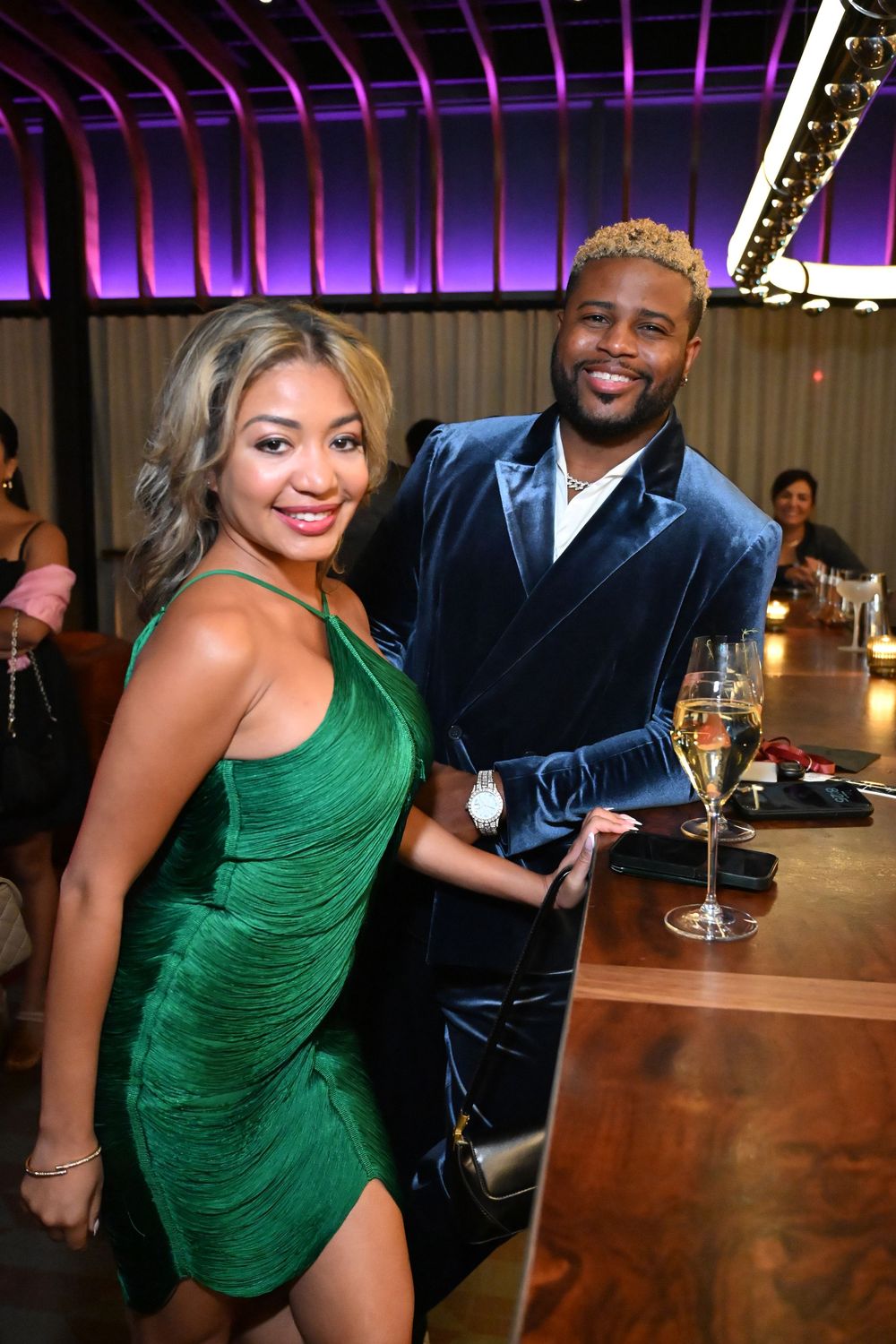 A couple poses together at a bar, with the woman wearing a vibrant green dress in multiple candid shots.