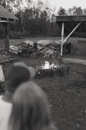 Black and white image of people watching a bonfire in an outdoor setting.
