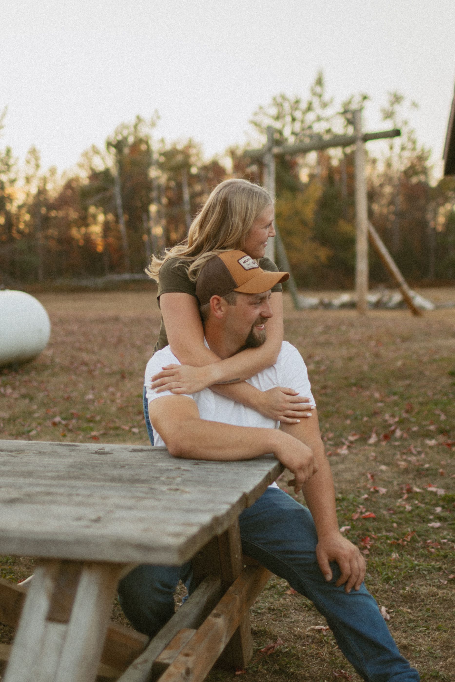 Couple sharing a playful piggyback ride moment by a picnic table outdoors.