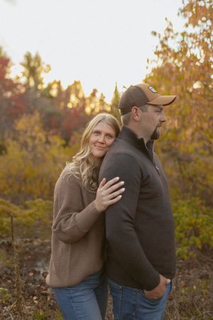 A couple shares an intimate moment outdoors against a backdrop of fall foliage.